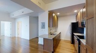 This 1-bedroom, 1-bathroom residence offers a thoughtfully designed single-floor layout that maximizes functionality within a compact footprint. The kitchen serves as a central feature of the space, showcasing warm-toned wood cabinetry that extends to the upper and lower sections, providing ample storage. A granite-topped peninsula with an undermount sink doubles as a prep and casual dining area, adding both practicality and visual appeal. Stainless steel and black appliances, including a refrigerator, complete the kitchen's contemporary aesthetic. A classic subway tile backsplash adds a clean, polished detail to the cooking area. The flooring throughout is warm hardwood, lending continuity and a welcoming atmosphere to the open-concept living and kitchen zones. Recessed lighting illuminates the space efficiently, complementing the natural light filtering in. Crisp white walls keep the interior feeling bright and open, while the open sightlines between the kitchen and living area enhance the overall sense of space. The unit's layout is practical and cohesive, making it well-suited for comfortable everyday living.
