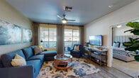 This well-designed single-floor residence offers a cohesive and inviting atmosphere with a consistent navy, gold, and neutral color palette carried throughout. The living room serves as the heart of the home, featuring wood-look flooring, a ceiling fan, and a sliding glass door that opens to a private balcony, flooding the space with natural light. A sectional sofa, upholstered armchair, and a rattan coffee table create a comfortable and stylish gathering area, complemented by large-scale wall art and elegant draping curtains.

The galley-style kitchen is efficiently laid out with dark espresso cabinetry, crisp white countertops, a stone tile backsplash, and a full suite of stainless and black appliances, including a refrigerator, range, and microwave. Light wood-look flooring keeps the space feeling bright and clean.

The primary bedroom is a serene retreat with plush carpeting, a ceiling fan, a tall upholstered headboard, and its own sliding door to a private balcony. The en-suite bathroom features a single vanity with a wide mirror and a walk-in shower. A second bedroom is thoughtfully configured with bunk beds and a built-in desk, making it ideal for multiple occupants. The second full bathroom includes a single vanity and a tub-shower combination.