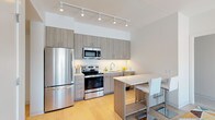 This single-floor residence offers a thoughtfully designed layout with modern finishes and urban views. The open-concept kitchen is outfitted with stainless steel appliances, including a French door refrigerator, electric range, and built-in microwave. Wood-toned cabinetry pairs with a white subway tile backsplash and light countertops, creating a clean, contemporary aesthetic. Track lighting illuminates the space, and a bar-height island with seating provides an ideal casual dining area. Light hardwood flooring extends throughout the main living areas.

The living room features large windows offering expansive city views, flooding the space with natural light. Two bedrooms are present, each with access to natural light and views of the surrounding cityscape. One bedroom includes a generous window framing skyline views, creating a bright, comfortable retreat.

Two bathrooms serve the residence, both finished with light tile flooring, wood-toned vanity cabinetry, and white countertops. One bathroom includes a tiled tub-shower combination. A dedicated in-unit laundry closet houses stacked Bosch washer and dryer units for added convenience. The overall design is clean and contemporary, with a neutral palette that contributes to a bright, cohesive atmosphere throughout.