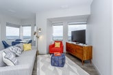 This single-floor residence is positioned at a notable elevation, offering sweeping panoramic views of the surrounding cityscape and beyond through large windows found throughout the unit. The open-concept living and dining area features wood-style flooring, abundant natural light, and a seamless layout that accommodates both relaxed lounging and casual dining. A dedicated dining nook sits adjacent to corner windows, maximizing the view.

The kitchen is outfitted with dark cabinetry, light quartz countertops, a subway tile backsplash, stainless steel appliances including a full-size refrigerator, range, and built-in microwave, and a central island with bar seating. The layout is efficiently designed for both cooking and entertaining.

The primary bedroom is carpeted and features large windows framing city views, while a second bedroom offers a similarly bright and airy feel. A flexible den space functions well as a home office, complete with built-in desk cabinetry and a sliding door for privacy.

Both bathrooms are finished with dark vanity cabinetry, white quartz countertops, and large-format tile flooring. The primary bath includes a glass-enclosed walk-in shower, while the secondary bath is clean and equally well-appointed.