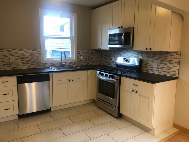 Gas range and over-the-range microwave/hood combo. Window overlooking back deck and yard. - 4842 NE Mallory Ave