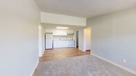 This single-floor residential unit offers a practical and well-organized layout designed for comfortable everyday living. The open-concept living and kitchen area serves as the heart of the space, where soft carpet in the living zone transitions to durable wood-look flooring in the kitchen. The kitchen is outfitted with crisp white cabinetry — both upper and lower — complemented by a light stone-pattern countertop, a double basin sink, a white electric range, and a full-size refrigerator. A flush-mounted ceiling light panel brightens the kitchen area effectively. The living area benefits from natural light provided by a window near the front entry door, which also features a wall-mounted HVAC unit for climate control. A dedicated bedroom offers carpeted flooring, a ceiling fan with light, a window overlooking the outdoors, a double-door closet, and direct access to the bathroom. The bathroom includes a single-sink vanity with white cabinetry, a toilet, and a full tub-shower combination with clean white surrounds and wood-look flooring. A separate utility closet houses the water heater. Throughout the unit, light gray walls, textured ceilings, and white trim create a clean, neutral aesthetic.