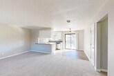 Located at 46745 Monroe St in Indio, California, this two-bedroom, two-bathroom single-floor residence offers a well-designed layout with a clean, neutral aesthetic throughout. The open-concept living area seamlessly connects the living room, dining space, and kitchen, creating a bright and cohesive gathering space. The kitchen features white cabinetry, a peninsula with a dark countertop, stainless steel appliances including a dishwasher, and wood-look flooring that extends into the kitchen and dining zone. A ceiling fan anchors the living area, which opens directly to a private balcony through sliding glass doors, allowing for natural light and outdoor views. Soft carpet covers the living room and both bedrooms, providing a comfortable feel underfoot. The spacious primary bedroom offers a dedicated closet with built-in hanging rods and a window for natural light. The second bedroom is equally well-proportioned with a large window and textured ceiling. Both bathrooms are fitted with clean white shower surrounds and chrome fixtures — one with a walk-in shower and the other with a shower-tub combination. A utility room and hallway round out the functional layout, making this a practical and comfortable home in the heart of the Coachella Valley.