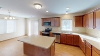 This single-level home is designed with a practical, open layout that connects the main living and kitchen areas seamlessly. The kitchen is a functional centerpiece, featuring warm medium-toned wood cabinetry extending to the ceiling, light stone countertops, a center island for additional prep space, and a full suite of stainless steel appliances including an electric range, built-in microwave, dishwasher, and refrigerator. Light hardwood-style flooring runs throughout the kitchen, complementing the neutral warm-beige walls found across the home.

The adjoining living area transitions to plush carpeting and receives natural light through a front-facing window and sliding glass door with vertical blinds. Ceiling fans with integrated light fixtures are present in multiple rooms, adding both comfort and illumination.

Bedrooms are carpeted and feature ceiling fans, natural light from windows, and wood-paneled sliding closet doors with built-in hanging rods. The bathrooms are finished with tile flooring in a warm stone pattern, wood-toned vanity cabinetry, white countertops, and tub-shower combinations with chrome grab bars. A dedicated laundry area houses a full-sized top-load washer and dryer, providing convenient in-unit laundry access.
