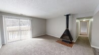 This single-floor unit offers a practical and comfortable layout across several well-defined rooms. The living room serves as the focal point of the space, highlighted by a striking black freestanding wood-burning stove set on a brick hearth, which draws the eye immediately upon entry. Soft wall-to-wall carpeting runs throughout the living and bedroom areas, lending warmth underfoot. A sliding glass door fitted with vertical blinds fills the living room with natural light and provides access to an outdoor area, bringing in views of the surrounding landscape.

The kitchen is designed in a galley configuration, featuring white cabinetry, gray laminate countertops, a stainless steel sink, and black appliances including an electric range and dishwasher. Durable wood-look vinyl flooring runs through the kitchen and continues into the bathroom and hallway areas.

The bedrooms are generously sized, each carpeted and accented with neutral gray walls and textured ceilings. Natural light enters through windows fitted with blinds, and closet space is provided for storage. One bedroom connects directly to the bathroom, offering added convenience.

The bathroom is equipped with accessibility features including grab bars near the toilet, a sliding glass-door shower stall, and wood-look vinyl flooring, making the space both functional and easy to navigate.