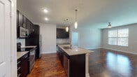 This single-floor residence offers a thoughtfully designed open-concept layout that seamlessly connects the kitchen, dining, and living areas. The kitchen serves as the centerpiece, featuring dark espresso cabinetry extending to the ceiling, granite countertops, a suite of stainless steel appliances including a refrigerator, microwave, and range, and a large center island with a built-in sink and pendant lighting overhead. Rich hardwood flooring runs throughout the main living areas, adding warmth and continuity to the space.

The living area is generously proportioned, filled with natural light from nearby windows, and accented by a ceiling fan. A dedicated nook with additional cabinetry and granite countertop provides a convenient built-in workspace or serving area just off the kitchen.

The bedrooms offer plush carpeting, natural light through blinded windows, and ceiling fans for comfort. The primary bedroom connects directly to an en-suite bathroom featuring hardwood floors, dark vanity cabinetry, granite countertops, and a large framed mirror. A spacious walk-in closet is also accessible from the primary bath. A secondary full bathroom mirrors the same finishes, complete with a tiled shower-tub combination and granite vanity, maintaining a cohesive aesthetic throughout the home.