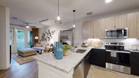 This thoughtfully designed single-floor residence offers a seamless blend of modern style and everyday functionality. The open-concept layout connects the kitchen and living area, creating a bright, cohesive space ideal for both relaxing and entertaining. The kitchen is a standout feature, boasting granite countertops, a central island with pendant lighting, dark lower cabinetry contrasted by light wood upper cabinets, a white subway tile backsplash, and stainless steel appliances including a range, microwave, and dishwasher. A deep single-basin sink and high-arc faucet add to the kitchen's practicality. The living area flows naturally from the kitchen, benefiting from natural light through large windows dressed with blinds and warm drapery. The bedroom is a calm retreat, featuring plush carpet flooring, a window with natural light, and ample room for furnishings. The bathroom is clean and contemporary, with light wood-look flooring, a granite-topped vanity with white cabinetry, a shower with a curtain enclosure, and a tall storage cabinet for added organization. Completing the residence is a dedicated in-unit laundry area housing a full-sized Whirlpool washer with overhead shelving. Wood-look flooring flows throughout the main living spaces, tying the home together with a warm, modern aesthetic.