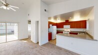 This single-floor, 2-bedroom, 1-bathroom residence offers a thoughtfully designed layout that maximizes both comfort and functionality. The open-concept living and kitchen area serves as the heart of the home, featuring soaring vaulted ceilings that lend an airy, spacious feel. The living room is finished with plush wall-to-wall carpeting and is anchored by a ceiling fan, with a large sliding glass door providing access to an outdoor area and filling the room with natural light. The kitchen is well-equipped with rich warm-toned wood cabinetry extending to the ceiling, grey laminate countertops, and white appliances including a range, microwave, refrigerator, and dishwasher. A kitchen island with additional counter space adds practicality. Both bedrooms are carpeted and feature vaulted ceilings, ceiling fans, and vertical blind-covered windows that allow natural light. The primary bedroom includes mirrored sliding closet doors, enhancing the sense of space. A hallway and dedicated closet provide additional storage. The bathroom is finished with neutral stone-look tile flooring, white cabinetry with a dark countertop vanity, a framed mirror, and a full soaking tub and shower combination, creating a clean and classic aesthetic throughout.
