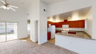 This single-floor, 2-bedroom, 1-bathroom residence offers a thoughtfully designed layout that maximizes both comfort and functionality. The open-concept living and kitchen area serves as the heart of the home, featuring soaring vaulted ceilings that lend an airy, spacious feel. The living room is finished with plush wall-to-wall carpeting and is anchored by a ceiling fan, with a large sliding glass door providing access to an outdoor area and filling the room with natural light. The kitchen is well-equipped with rich warm-toned wood cabinetry extending to the ceiling, grey laminate countertops, and white appliances including a range, microwave, refrigerator, and dishwasher. A kitchen island with additional counter space adds practicality. Both bedrooms are carpeted and feature vaulted ceilings, ceiling fans, and vertical blind-covered windows that allow natural light. The primary bedroom includes mirrored sliding closet doors, enhancing the sense of space. A hallway and dedicated closet provide additional storage. The bathroom is finished with neutral stone-look tile flooring, white cabinetry with a dark countertop vanity, a framed mirror, and a full soaking tub and shower combination, creating a clean and classic aesthetic throughout.