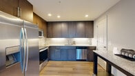 Located in McLean, Virginia, this thoughtfully designed one-bedroom, one-bathroom residence offers a modern aesthetic with quality finishes throughout. Light-toned hardwood-style flooring runs continuously through the main living areas, creating a cohesive and airy feel. The open-concept living and dining area is bathed in natural light from large floor-to-ceiling windows and sliding glass doors that open to a private balcony, offering serene treetop views. The kitchen is a standout feature, showcasing rich dark cabinetry with under-cabinet lighting, light granite countertops, stainless steel appliances including a refrigerator, range, microwave, and dishwasher, and a functional island for additional prep space. The bedroom is a comfortable and calm retreat, featuring large windows that frame lush green canopy views, providing a tranquil atmosphere. The full bathroom is finished with granite countertops, a dark wood vanity, a framed mirror, and clean tile flooring. A dedicated walk-in closet with a full wire shelving system provides generous, well-organized storage. Two hallways connect the rooms efficiently, contributing to the smooth, functional layout of this well-appointed McLean residence.