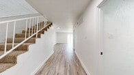 This two-story residence is designed with a clean, contemporary aesthetic, featuring a consistent white color palette, textured ceilings, and wood-look laminate flooring across the main level. The entry foyer leads into an open living area illuminated by natural light from a large sliding glass door fitted with vertical blinds. A staircase with a white metal railing connects to the upper floor, where carpet continues into the bedrooms.

The galley-style kitchen is well-appointed with white cabinetry featuring matte black hardware, light stone countertops, a stainless steel sink, and stainless appliances including an electric range and refrigerator. A skylight panel overhead adds additional brightness to the space.

A half bathroom on the main level includes a white vanity with a granite-style countertop, a black-framed mirror, and matte black fixtures. Upstairs, the bedrooms are carpeted and each features a ceiling fan with light kit, a window for natural light, and closet access. The upper-level full bathroom includes a white vanity, wood-look flooring, and a tub-shower combination. Throughout, the space maintains a neutral, move-in-ready presentation.