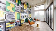 Located at 3230 Kinsrow Ave in Eugene, Oregon, this dynamic community amenity space at The Flats @ Chase is designed with University of Oregon pride and modern functionality in mind. The layout flows across a single level, connecting distinct zones that serve both social and productive purposes.

The lounge area makes an immediate impression with soaring double-height ceilings and a dramatic floor-to-ceiling photo mural collage celebrating University of Oregon athletics and campus life in signature green and yellow. Plush emerald velvet sofas, cognac leather chairs, gold accent tables, and a sculptural branching chandelier create a stylish, welcoming gathering space. Large windows flood the room with natural light and offer views of the surrounding greenery.

Adjacent to the lounge, a co-working area provides a built-in wooden countertop bar with sleek black seating, ideal for studying or remote work, bathed in natural light from expansive windows overlooking an outdoor terrace furnished with patio seating.

The fully equipped communal kitchen features dark cabinetry, white quartz countertops, a patterned tile backsplash, stainless steel appliances including a French door refrigerator, range, and dishwasher, open wood shelving, and a large central island with pendant lighting—perfect for group gatherings and entertaining. Wood-look flooring runs throughout, tying the entire space together with warmth and cohesion.