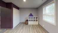 This single-floor fitness and yoga studio is thoughtfully designed to support an active and mindful practice. The space features a clean, modern aesthetic defined by a striking two-tone color scheme: deep plum accent walls paired with soft grey surfaces that create an energizing yet calming atmosphere throughout.

Light wood-look luxury vinyl plank flooring runs seamlessly across the entire studio, providing a smooth, durable surface well-suited for yoga, stretching, and movement-based activities. A large floor-to-ceiling mirror spans one wall, visually expanding the room while allowing practitioners to monitor their form during sessions. Complementing this, a wall-mounted flat-screen television is positioned for easy viewing, supporting guided workouts or instructional content.

Natural light enters through multiple windows fitted with horizontal blinds, brightening the space and creating an inviting environment. A dedicated storage area features a white cube shelving unit stocked with yoga blocks and accessories, alongside a woven basket for additional organization. A standard closet provides further storage capacity.

The overall layout is open and uncluttered, offering ample floor space for multiple yoga mats simultaneously, making it suitable for both individual sessions and small group classes.