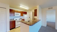 This single-floor residence offers a well-organized layout designed for comfortable everyday living. The kitchen is equipped with warm wood cabinetry, granite-look countertops, white appliances including an electric range, microwave, and refrigerator, and is finished with easy-to-clean tile flooring. A peninsula breakfast bar connects the kitchen to the adjoining living area, providing both additional counter space and a casual dining option. A walk-in pantry with wire shelving adds generous storage directly off the kitchen. The living room is spacious and carpeted, featuring a ceiling fan and a sliding glass door that opens onto a private balcony, allowing for natural light and outdoor views. The bedrooms are carpeted and bright, each benefiting from large windows that frame pleasant outdoor scenery and ceiling fans for comfort. The bathroom is clean and functional, featuring tile flooring, a wood-toned vanity with a granite-look countertop, a large mirror with overhead lighting, and a full tub-shower combination with white tile surround. A dedicated laundry area accommodates a full-size washer and dryer and includes built-in wire shelving for added storage. Throughout the unit, neutral tones and consistent finishes create a cohesive and practical living environment.