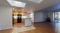 Located in the Encino neighborhood of Los Angeles, this single-floor residence at 4940 Paso Robles Ave offers a well-designed, open layout that maximizes comfort and functionality. The heart of the home is an open-concept kitchen and living area, where warm wood cabinetry, white countertops, and black appliances — including a gas range and over-the-range microwave — are complemented by a striking skylight overhead that floods the space with natural light. A central kitchen island provides additional prep and gathering space, flowing seamlessly into the open living area with rich hardwood flooring throughout. A dedicated dining area is distinguished by elegant pendant lighting, adding a refined touch to everyday meals. The bedrooms are generously proportioned, each featuring hardwood floors, ample closet space with mirrored sliding doors, and access to natural light. One bedroom includes a sliding glass door opening to an outdoor view, adding a bright, airy quality to the space. Both bathrooms are finished with warm wood vanities, white countertops, and tiled tub-shower combinations enclosed by glass sliding doors, set on earthy stone-look tile flooring. Clean lines, neutral tones, and recessed lighting throughout contribute to a cohesive, inviting ambiance across the entire residence.
