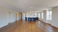 Located at 115 Lake St in Libertyville, IL, this single-floor residence offers a thoughtfully designed open-concept layout that seamlessly connects the living and kitchen areas. Rich hardwood flooring extends throughout the main living space, enhancing the bright, airy atmosphere created by multiple large windows that invite abundant natural light and views of the surrounding neighborhood.

The kitchen is a standout feature, equipped with two-tone cabinetry — crisp white upper cabinets paired with dark lower cabinets — complemented by open shelving with black iron brackets, a white subway tile backsplash, quartz countertops, stainless steel sink, and a gas range. A large navy-blue center island anchors the space, while pendant lighting adds a refined touch overhead.

The bedrooms are finished with plush carpeting for comfort, and one includes a walk-in closet and private en-suite bath. The en-suite bathroom showcases a glass-enclosed walk-in shower with a rain showerhead, hexagonal tile flooring, and an open-shelf wood vanity with white quartz countertops. A secondary bathroom features a wood-toned vanity with brass hardware and classic hexagonal tile flooring. Recessed lighting throughout ensures consistent, modern illumination across all spaces.