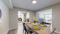 This single-floor residence at 9415 Doral Ct in Louisville, Kentucky offers a well-designed, functional layout that flows naturally between living, dining, and kitchen spaces. The living room is bright and welcoming, featuring durable wood-look flooring, a textured ceiling, and a large sliding glass door with vertical blinds that fills the room with natural light and provides direct access to the outdoors. The adjacent dining area comfortably accommodates a full-size dining table and connects seamlessly to the kitchen. The kitchen is equipped with white shaker-style cabinetry, dark countertops, subway tile backsplash, and stainless steel appliances including a range, refrigerator, and dishwasher. Two bedrooms feature plush carpet flooring and ceiling fans, offering a quiet and comfortable retreat. The primary bedroom provides generous space for furniture arrangement, while the secondary bedroom includes a window with natural light. The bathroom is cleanly appointed with a white vanity, tiled tub-shower combination, and wood-look flooring. Throughout the home, neutral gray tones and consistent flooring choices create a cohesive and modern aesthetic suited to a variety of lifestyles.