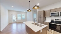 Located at 34040 W 90th St in De Soto, Kansas, this thoughtfully designed 2-bedroom, 2-bathroom unit offers a comfortable and modern single-floor layout. The open-concept kitchen serves as a central highlight, featuring warm taupe shaker-style cabinetry, white quartz countertops, a center island with a sink, stainless steel appliances including a refrigerator, range, and over-the-range microwave, and stylish pendant lighting over the island. Light wood-style flooring runs throughout the main living areas, creating a clean and cohesive aesthetic. Both bedrooms are carpeted and bathed in natural light through multiple windows with blinds, each equipped with ceiling fans for added comfort. The primary bedroom includes access to a dedicated closet and a well-sized en-suite bathroom featuring warm wood cabinetry, white countertops, and light wood flooring. The second bathroom mirrors a similar refined design. Two closets provide ample storage throughout the unit. A dedicated laundry room houses a full-size washer and dryer, adding significant everyday convenience. The overall ambiance is bright, clean, and modern, with a neutral color palette that lends itself to a welcoming and versatile living environment.
