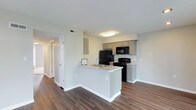 Located at 4075 Alkire Glen Way in Columbus, Ohio, this single-floor residence offers a clean, modern aesthetic with a thoughtfully designed open-concept layout. The kitchen serves as a central highlight, featuring gray shaker-style cabinetry, a classic white subway tile backsplash, and light granite countertops that extend across a peninsula with a built-in sink. Black appliances, including a refrigerator, range, and over-the-range microwave, complement the contemporary palette. The peninsula creates a natural division between the kitchen and the adjoining living area, making the space feel both functional and connected. Rich, dark hardwood-style flooring flows throughout, adding warmth and contrast to the light gray walls and crisp white trim. Flush-mounted ceiling lighting provides even illumination throughout the open areas, while multiple doorways visible from the main living space hint at well-organized private rooms beyond. Neutral tones dominate the interior, offering a versatile backdrop that suits a variety of furnishing styles. The overall ambiance is fresh, bright, and move-in ready, reflecting a balance of practical design and modern residential comfort.
