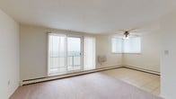 This single-floor residence offers a thoughtfully arranged layout that balances open living spaces with functional private areas. The living room serves as the centerpiece of the unit, featuring a generous carpeted area, a ceiling fan, and large sliding glass doors fitted with vertical blinds that open onto a balcony, providing outdoor views and abundant natural light. A secondary window in the corner further brightens the space. Baseboard heating runs throughout, ensuring consistent comfort.

The kitchen is well-appointed with rich, medium-toned wood cabinetry, dark granite countertops, and a neutral tile backsplash. Stainless steel appliances—including a gas range, over-the-range microwave, dishwasher, and refrigerator—complete the space. Light tile flooring extends through the kitchen and into the entryway.

Two carpeted bedrooms offer quiet retreats, each with windows that invite natural light and baseboard heating units below. The unit includes two bathrooms: one featuring white tile flooring, a vanity, and a tub-shower combination, while the second offers warm beige tile walls and flooring with a glass-enclosed standing shower and a wood-toned vanity, presenting a more refined aesthetic.