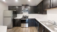 This single-floor residence offers a clean, contemporary design throughout, combining practical functionality with modern finishes. The kitchen serves as a standout feature, showcasing rich dark cabinetry with sleek hardware, crisp white countertops, and a full suite of stainless steel appliances including a range, over-the-range microwave, and dishwasher. Light wood-tone flooring runs through the kitchen and connects seamlessly to the main living areas, while an arched passageway adds an architectural touch to the layout. The bedrooms are finished with soft wall-to-wall carpeting and each includes a ceiling fan with integrated lighting and a generously sized window that brings in natural light. One bedroom features a spacious walk-in closet outfitted with wire shelving, providing ample storage. The bathrooms maintain a consistent design language, featuring dark vanity cabinetry, white countertops with undermount sinks, and full tub-shower combinations with built-in shelving. Wood-look flooring and recessed lighting complete the clean, bright aesthetic of the bathrooms. Throughout the space, white walls, white panel doors with brushed nickel hardware, and crisp baseboards create a cohesive, move-in-ready environment that is both functional and inviting.