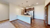 This thoughtfully designed 2-bedroom, 2-bathroom single-floor residence offers a functional and modern layout. The open-concept kitchen and living area serves as the heart of the home, anchored by a generous kitchen island with a white quartz countertop, an undermount sink, and elegant pendant lighting. Rich dark-stained cabinetry pairs seamlessly with stainless steel appliances, including a refrigerator, microwave, and dishwasher, while durable hardwood-style flooring ties the space together. The living area flows naturally from the kitchen, featuring soft carpet, neutral sage-green accent walls, and access to natural light through multiple windows.

The two bedrooms are carpeted and bright, with the primary bedroom offering a ceiling fan and a walk-in closet with built-in shelving for organized storage. The second bedroom also receives ample natural light. Both bathrooms are clean and functional, with one featuring a full soaking tub, brushed nickel fixtures, and a safety grab bar. A dedicated in-unit laundry room with a full-size washer and dryer adds everyday convenience. With three total closets, recessed lighting throughout, and warm wood-trimmed doors and baseboards, this residence balances practicality with polished, contemporary finishes.