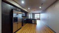This single-floor residence offers a thoughtfully designed open-concept layout that maximizes both functionality and style. Warm-toned hardwood flooring flows throughout the main living areas, creating a cohesive and inviting atmosphere. The kitchen is a standout feature, outfitted with a full suite of stainless steel appliances — including a side-by-side refrigerator with ice maker, electric range, built-in microwave, and dishwasher — all complemented by rich dark cabinetry, a tile backsplash, and granite countertops. A peninsula with pendant lighting above serves as a natural divider between the kitchen and the open living area, which is illuminated by recessed lighting throughout. The bedroom is carpeted for comfort and features a ceiling fan, a generous walk-in closet with wire shelving, and a large sliding glass door opening to a private balcony with panoramic city views. An additional room with hardwood flooring and a sizable window also captures scenic outdoor views. The bathroom is finished with floor-to-ceiling subway tile surrounding a soaking tub and shower combination with a glass panel door, paired with a dark vanity and tile flooring. Throughout the space, neutral wall tones and clean architectural lines contribute to a modern, urban aesthetic.