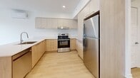 Located at 3250 Boulevard Henri-Bourassa Est in Montréal, this thoughtfully designed 3-bedroom, 1-bathroom unit offers a contemporary and functional layout across a single floor. The open-concept kitchen serves as a central highlight, featuring a large island with an integrated sink, stainless steel appliances including a refrigerator and range, and dual-tone cabinetry in light wood and matte grey with ample upper and lower storage. Recessed lighting illuminates the space, complemented by light hardwood flooring that runs throughout. The living and kitchen areas flow cohesively, creating a welcoming and practical common space. Each of the three bedrooms is bright and clean, finished with the same light hardwood floors and crisp white walls. Two bedrooms feature large windows overlooking the surrounding urban streetscape, filling the rooms with natural light and views of the neighbourhood. The primary bedroom includes a sliding closet door for efficient storage. The bathroom is finished with light wood cabinetry, a white undermount sink, a wall-mounted mirror, a tall storage cabinet, and tile flooring, offering a clean and modern aesthetic. Baseboard heating is present throughout, and the overall design maintains a neutral, contemporary palette ideal for a variety of living arrangements.