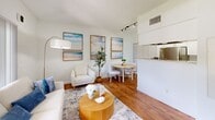 Located in Miami, FL, this well-appointed one-bedroom, one-bathroom residence offers a thoughtfully organized single-floor layout. The open living area is bright and welcoming, featuring warm hardwood flooring, a large window that invites natural light and outdoor views, and a textured ceiling. The space is accented with coastal-inspired artwork and a comfortable seating arrangement centered around a round wooden coffee table, creating an inviting atmosphere. A compact dining nook sits adjacent to the living area, seamlessly connecting to the kitchen. The kitchen is efficiently designed with crisp white cabinetry, granite-style countertops, a stainless steel sink, and modern appliances including an electric range, making it both functional and attractive. The bedroom is a calm retreat, featuring plush carpeting, a ceiling fan, a window with garden views, and vibrant wall art above the bed that adds a splash of color to the neutral palette. The bathroom is clean and practical, finished with white tile, a tub-shower combination, white cabinetry with overhead storage, and hardwood-style flooring. Throughout the residence, a consistent light and airy color scheme, along with warm wood floors in the main living spaces, ties the home together into a cohesive and comfortable living environment.
