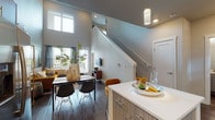 This two-story residence makes a striking first impression with its dramatic double-height ceilings in the main living area, creating an expansive, airy atmosphere. The open-concept layout on the main floor seamlessly connects the living, dining, and kitchen areas. A staircase rises prominently from the main floor, serving as both a functional and architectural element.

The kitchen is outfitted with light wood cabinetry, a slate-toned subway tile backsplash, stainless steel appliances, and a white quartz island with bar seating. Dark hardwood flooring runs throughout the main level, complementing the contemporary aesthetic. Large windows flood the living area with natural light and offer outdoor views, while the soaring walls provide ample space for décor.

Upstairs, the bedrooms feature angled ceilings that follow the roofline, plush carpeting, and generous closet space. A secondary room offers flexibility as a home office or additional bedroom, complete with an outdoor-facing window. The bathroom includes a full tub-shower combination with dark tile surround, a sleek vanity, and wood-look flooring, maintaining the modern design language found throughout the home.