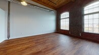 Located at 205 Esten Ave in Pawtucket, Rhode Island, this two-floor loft-style unit showcases a compelling blend of historic industrial character and contemporary updates. The main level greets you with rich hardwood flooring, soaring wood-planked ceilings, and exposed brick walls that speak to the building's storied past. An arched window allows natural light to pour into the open living area, while visible ductwork overhead adds to the authentic loft aesthetic. A structural wood post anchors the central space, which flows seamlessly into the kitchen. The kitchen is well-appointed with dark cabinetry, granite countertops, stainless steel appliances including a refrigerator, electric range, and dishwasher, and hardwood floors that carry through from the main living area. A mezzanine-level loft, accessible via an interior staircase and framed by a sleek metal railing, provides an additional versatile space featuring original wide-plank wood flooring and continued wood-plank ceilings. This upper level overlooks the main living area below, enhancing the sense of openness and volume throughout. The bathroom features a full soaking tub with a tiled surround in a neutral, multi-toned mosaic pattern, complemented by tile flooring, offering a clean and polished finish.