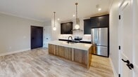 Located at 401 Cherry Ave in Charlottesville, Virginia, this single-floor residence combines contemporary design with functional living spaces. Light-toned hardwood-style flooring runs consistently throughout, creating a cohesive and airy aesthetic across every room.

The kitchen serves as the centerpiece of the unit, showcasing bold dark cabinetry with brass hardware set against a textured tile backsplash. A large island with a natural wood base and bright white quartz countertop anchors the space, fitted with an undermount sink and matte black faucet. Stainless steel appliances, including a range with a wall-mounted hood and a French door refrigerator, add a polished touch. Globe pendant lights suspended from above provide warm, stylish illumination.

The living area is generously proportioned and bathed in natural light from multiple windows, with a glass-panel door leading to an outdoor balcony area. Bedrooms are well-sized, each with ceiling fans, natural light from surrounding windows, and ample closet storage.

The bathroom features a glass-enclosed walk-in shower with white subway tile, dark hexagon accent tile, matte black fixtures, and a floating wood vanity with a white countertop, blending clean lines with upscale detail throughout.