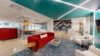 This expansive single-floor commercial office space spans a generous 5,000 square feet, masterfully combining industrial and contemporary design elements to create a dynamic and energizing work environment. The layout opens into a welcoming lounge area anchored by a bold red velvet sofa, white accent chairs, and a striking teal-painted ceiling with integrated linear LED lighting — a vivid focal point that sets the tone for the entire space. Polished concrete floors flow throughout, lending a sleek, cohesive feel underfoot. Glass-walled conference and meeting rooms line the perimeter, offering visual transparency while maintaining acoustic separation, and are appointed with warm wood accents and modern furnishings. A centrally located kitchen and bar area features a white quartz island with mustard yellow barstools, warm wood cabinetry, teal tile backsplash, and pendant lighting cascading from an exposed ceiling with visible ductwork — a nod to the space's industrial character. A mezzanine-level seating nook with Edison bulb pendants and a steel cable railing provides an intimate perch above the main floor. A bright, window-lined lounge at the far end invites natural light deep into the space, complemented by a vibrant rainbow-patterned area rug and comfortable soft seating. Private offices and focus rooms with wood doors round out a well-balanced, thoughtfully designed workplace.