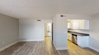 This single-floor unit offers a clean, functional layout designed for comfortable everyday living. The open living area is finished with durable wood-look flooring in warm tones, neutral gray walls, and a textured ceiling, creating a bright and airy atmosphere. A wide window in the living space allows natural light to fill the room, enhancing the sense of openness.

The kitchen is efficiently designed with white cabinetry, open shelving, dark countertops, and stainless steel appliances including a refrigerator and dishwasher. The layout maximizes counter and storage space, making it practical for daily use. Wood-look flooring continues seamlessly from the living area into the kitchen.

A hallway connects the main living space to the bathroom and additional rooms. The bathroom features a full tub-shower combination with a curved curtain rod, a grab bar for added accessibility, and a white vanity with a single sink, stone-look countertop, and a mirror with wall lighting. A separate storage closet is accessible from the bathroom hallway, providing ample organizational space. Throughout the unit, consistent finishes including white trim, neutral paint tones, and updated flooring contribute to a cohesive and move-in-ready aesthetic.