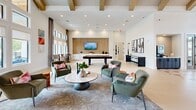Located at 10191 Main St in Houston, TX, this single-story community facility spans an impressive 5,200 square feet of thoughtfully designed space. The grand entrance welcomes visitors beneath soaring vaulted ceilings with exposed wood beam detailing and a striking multi-light chandelier, while a boldly patterned geometric floor adds visual interest throughout the open main hall. Large windows flood the space with natural light, creating a bright and inviting atmosphere.

The lounge area features a sophisticated layout with plush green velvet seating, a central coffee table, and a bar-height counter with pendant lighting — ideal for gathering and socializing. A dedicated mailroom is outfitted with multiple organized mailbox kiosks set within shiplap-clad white islands, accented by modern circular pendant lights.

Three private offices provide functional meeting spaces, each distinctly appointed — one with a light wood conference table and frosted glass partitions, another with green upholstered chairs and oversized drum pendant lights with outdoor views.

The fully equipped fitness center is a standout feature, boasting vaulted wood-beamed ceilings, a wide array of strength and cardio machines, floor-to-ceiling mirrors, and TRX suspension equipment. Clean, well-lit hallways with tasteful artwork and a dual water fountain station connect all areas seamlessly. Two bathrooms complete the facility.