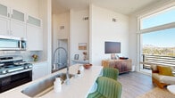 This well-appointed 2-bedroom, 1-bathroom residence offers a thoughtfully designed single-floor layout that maximizes both space and functionality. The open-concept living and kitchen area is anchored by dramatically high ceilings that create an airy, expansive atmosphere throughout. Large floor-to-ceiling windows in the living room frame sweeping panoramic views of the surrounding landscape, including distant mountain scenery, while flooding the space with abundant natural light. Light-toned hardwood flooring runs consistently throughout the unit, reinforcing a clean, cohesive aesthetic.

The kitchen is a standout feature, equipped with stainless steel appliances including a French door refrigerator and gas range, white shaker-style cabinetry extending to the ceiling with frosted glass upper panels, a light quartz countertop island with bar seating, and a tile backsplash. A dedicated dining area adjoins the kitchen, providing a functional yet stylish space for meals.

Both bedrooms benefit from sliding glass doors that open to a private balcony with mountain and city views. The primary bedroom includes a spacious walk-in closet with wire shelving for ample storage. A secondary room with hardwood floors offers flexible use as a bedroom or office. The bathroom and a well-organized walk-in closet round out this refined, modern residence.