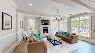 Located at 700 Gates Mills Dr in Fort Mill, SC, this single-story community clubhouse offers a thoughtfully designed layout across a generous footprint. The welcoming entrance foyer features rich hardwood flooring, decorative columns, crown molding, and a chandelier overhead, flanked by reception desks that set a polished, professional tone.

The primary living room is a bright, open gathering space anchored by a floor-to-ceiling tiled fireplace with a wall-mounted TV above. Large multi-pane windows flood the room with natural light and offer views of the outdoor community amenity area. Crown molding, hardwood floors, and a statement chandelier enhance the refined ambiance.

A second living area provides a more casual lounge setting, complete with a media console, wall-mounted TV, and textured area rug. Adjacent to these spaces is an intimate dining nook featuring a live-edge wood table, built-in bench seating, a statement pendant light, and a wall-mounted display screen — ideal for small gatherings or meetings.

The kitchen and living room combination showcases dark espresso cabinetry, granite countertops, a mosaic tile backsplash, stainless steel appliances, and an oversized curved island with pendant lighting and bar seating. Light-toned tile flooring and glass-paneled doors connect the private rooms, completing this versatile and elegantly finished community space.