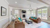 Located at 700 Gates Mills Dr in Fort Mill, SC, this single-story community clubhouse offers a thoughtfully designed layout across a generous footprint. The welcoming entrance foyer features rich hardwood flooring, decorative columns, crown molding, and a chandelier overhead, flanked by reception desks that set a polished, professional tone.

The primary living room is a bright, open gathering space anchored by a floor-to-ceiling tiled fireplace with a wall-mounted TV above. Large multi-pane windows flood the room with natural light and offer views of the outdoor community amenity area. Crown molding, hardwood floors, and a statement chandelier enhance the refined ambiance.

A second living area provides a more casual lounge setting, complete with a media console, wall-mounted TV, and textured area rug. Adjacent to these spaces is an intimate dining nook featuring a live-edge wood table, built-in bench seating, a statement pendant light, and a wall-mounted display screen — ideal for small gatherings or meetings.

The kitchen and living room combination showcases dark espresso cabinetry, granite countertops, a mosaic tile backsplash, stainless steel appliances, and an oversized curved island with pendant lighting and bar seating. Light-toned tile flooring and glass-paneled doors connect the private rooms, completing this versatile and elegantly finished community space.