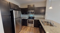 This single-floor unit offers a thoughtfully designed layout that balances functionality and comfort throughout. The kitchen is a standout feature, showcasing rich dark espresso cabinetry, granite countertops, and a full suite of stainless steel appliances including a refrigerator, electric range, and over-the-range microwave. Warm hardwood-style flooring runs throughout the kitchen, which also includes a peninsula breakfast bar with pendant lighting overhead — an ideal space for casual dining or entertaining.

The open-concept living area flows seamlessly from the kitchen, featuring plush carpeting, neutral wall tones, and a ceiling fan. A glass-paned door with flanking windows fills the living space with natural light and provides direct access to the outdoors.

The bedrooms are comfortably sized, each with plush carpet, ceiling fans, and ample natural light from well-positioned windows with blinds. The primary bedroom connects directly to a private en-suite bathroom, which features a dark-toned vanity with a white countertop, tile flooring, and a glass-enclosed shower. A spacious walk-in closet is accessible directly from the bathroom, offering generous storage. An additional closet in the primary bedroom provides even more organizational flexibility. The unit's neutral color palette and clean finishes create a cohesive, move-in-ready aesthetic throughout.