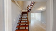 Located at 24 Claremont Gardens in Ossining, NY, this two-story residence offers a well-organized layout spread across two floors. The main level features a living room with large windows that invite abundant natural light and views of surrounding greenery, alongside a dedicated dining room and a galley-style kitchen fitted with dark gray cabinetry, stainless steel appliances including a gas range and refrigerator, light countertops, and a window that brightens the workspace. Light wood-tone flooring flows throughout both levels, lending a clean and cohesive aesthetic. A striking open-tread staircase with rich wood steps and a black metal railing serves as a visual centerpiece, connecting the main floor to the upper level. The upper floor hosts both bedrooms, including a primary bedroom distinguished by vaulted ceilings, a sliding-door closet, and windows overlooking lush tree canopy. The second bedroom is well-proportioned with ample natural light and a similarly airy feel. Four closets throughout the home provide generous storage. The shared full bathroom features tile flooring, a dark wood vanity, a wall-mounted mirror, and a tub-shower combination. Hallways and multiple staircase access points ensure smooth circulation throughout the home.