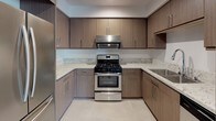 This single-floor residence is designed with a clean, contemporary aesthetic that carries consistently through each space. The kitchen is a standout feature, outfitted with flat-front cabinetry in a warm taupe wood-grain finish, light speckled granite countertops, and a full suite of stainless steel appliances, including a gas range with overhead ventilation, a French-door refrigerator, and a built-in microwave. Large-format tile flooring and a built-in counter nook add both practicality and style to the kitchen area.

The open layout connects the kitchen to a living area finished with warm wood-tone flooring, providing a cohesive and inviting atmosphere. Multiple doors lead to the bedrooms, one of which features soft carpeting and a window with an exterior view, allowing natural light to fill the room.

The unit includes two bathrooms, both finished in a bright, minimalist style with white walls, light tile flooring, and light wood vanity cabinetry paired with white countertops and frameless mirrors. One bathroom offers an extended vanity with additional storage, while the other features a compact single-sink vanity with clean chrome fixtures. Both spaces convey a sense of calm functionality consistent with the overall design of the residence.