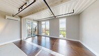 Located at 2150 Byrum Ave in Nashville, TN, this one-bedroom unit offers a distinctive industrial-chic aesthetic rooted in its repurposed shipping container architecture. The corrugated metal ceiling panels, exposed structural elements, and rich hardwood flooring create a raw yet refined character throughout the living space.

The open-plan kitchen is well-appointed with a full suite of stainless steel appliances, including a French door refrigerator, electric range, built-in microwave, and dishwasher. White cabinetry is complemented by open metal shelving, providing both style and functionality. A wall-mounted mini-split system ensures climate control throughout the unit.

The bedroom features neutral gray walls, dark hardwood flooring, and a tall window that frames lush greenery and open sky views, filling the room with natural light. A dedicated mini-split unit keeps the room comfortable year-round.

The living area includes generous closet storage and a conveniently located in-unit laundry alcove. Industrial-style track lighting overhead enhances the contemporary feel of the space.

A standout feature is the expansive rooftop deck, accessible from the unit, offering sweeping views of the Nashville skyline and surrounding treetops. The deck is finished with composite decking, black metal railings, and a built-in outdoor media cabinet, making it an exceptional outdoor entertaining space.