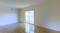This single-floor space offers a clean, minimalist layout with a welcoming sense of openness. The main living area is finished with polished light hardwood floors that reflect natural light beautifully, contributing to the bright and airy atmosphere throughout. Crisp white walls provide a neutral backdrop that enhances the sense of spaciousness and allows for versatile interior design possibilities.

A prominent sliding glass door serves as a key architectural feature, flooding the room with abundant natural light while providing direct access to an outdoor balcony. The balcony is framed with a classic railing and overlooks lush surrounding trees, offering a pleasant outdoor retreat and a connection to nature. The views of mature greenery through the glass door create a calm and inviting ambiance even from within the interior.

The smooth, uniform ceiling height maintains a consistent, comfortable scale across the space. Overall, the combination of gleaming hardwood floors, sun-drenched interiors, and seamless indoor-outdoor access makes this a practical yet appealing space well-suited for a variety of uses.