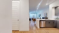 This thoughtfully designed 1-bedroom, 2-bathroom residence offers a cohesive open-concept layout across a single floor, maximizing every square foot with clean, contemporary finishes. Light hardwood flooring flows seamlessly throughout the space, creating a warm and unified aesthetic.

The kitchen is a standout feature, outfitted with sleek gray cabinetry, white quartz countertops, white subway tile backsplash, and a full suite of stainless steel appliances including a refrigerator, range, microwave, and dishwasher. A peninsula provides additional prep space and opens directly to the dining area, which comfortably accommodates a round dining table. Recessed lighting illuminates both zones effectively.

The living room is bright and airy, benefiting from large windows dressed with sheer curtains that allow abundant natural light while maintaining privacy. The bedroom is a serene retreat, featuring large windows with outdoor views, a ceiling fan, and access to a dedicated en-suite bathroom. This bathroom includes a gray vanity with white countertop, modern matte black fixtures, and a lighted mirror. A second full bathroom features a soaking tub with large-format tile surround and matte black hardware. The unit is completed by a dedicated closet, offering practical storage solutions.