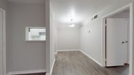 This single-story, one-bedroom, one-bathroom unit offers a thoughtfully arranged layout that maximizes its compact footprint. Throughout the space, dark hardwood-style flooring contrasts cleanly with light gray walls and crisp white baseboards, creating a cohesive, modern aesthetic.

The living area is open and straightforward, anchored by a pendant light fixture and a textured ceiling. A pass-through window connects this space directly to the kitchen, enhancing the sense of openness. The front entry opens naturally into the living area, with the kitchen positioned just off to the side.

The galley-style kitchen is efficiently designed, featuring gray cabinetry, a tile backsplash, a stainless steel refrigerator, a gas range, a dishwasher, and a single-basin sink. Cabinet storage extends to the upper and lower walls, providing practical organization throughout.

The bedroom is a calm, well-proportioned room with the same dark flooring, neutral gray walls, and a window fitted with blinds that allows natural light while maintaining privacy.

The bathroom includes a full tub-and-shower combination with white tile surround, a toilet, and a vanity, all finished in clean, neutral tones consistent with the rest of the unit.