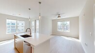 Located at 1153 Bees Ferry Rd in Johns Island, SC, this thoughtfully designed single-floor home offers three bedrooms, two bathrooms, and a well-organized layout that balances comfort and modern style. The open-concept kitchen and living area serves as the heart of the home, anchored by a large center island with a white quartz countertop, undermount sink, and warm natural wood cabinetry. Pendant lighting and recessed fixtures illuminate the space, while multiple windows bathe the living area in natural light. Light-toned wood-look flooring runs throughout the main living areas, adding to the clean, contemporary aesthetic. The primary bedroom features plush carpeting, a ceiling fan, and generous natural light through a large window, accompanied by a spa-inspired en-suite bathroom with a double vanity, light wood cabinetry, white quartz countertops, and a glass-enclosed marble-tile shower. Secondary bedrooms also offer soft carpeting and ceiling fans. A dedicated mudroom with built-in shelving, hooks, and a bench provides practical everyday organization. Three closets, including a walk-in with wire shelving, offer ample storage. The home's bright, neutral palette and modern finishes create a clean, inviting atmosphere throughout.