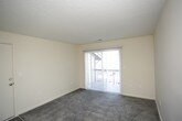 This single-floor unit offers a practical and comfortable layout with a clean, neutral aesthetic throughout. The living area is carpeted in a medium-toned grey and features a sliding glass door dressed with vertical blinds, allowing natural light to filter in while providing access to an outdoor space. A textured ceiling runs throughout the common areas, adding a subtle design element overhead.

The kitchen is efficiently arranged with white cabinetry lining both walls, providing generous storage both above and below the countertops. Granite-style countertops offer durable workspace alongside a double stainless steel sink. White appliances, including a freestanding coil-burner range with an overhead exhaust hood and a full-size refrigerator, complete the kitchen setup. Wood-look flooring in a warm grey tone runs through this space, contrasting neatly with the cabinetry. An electrical panel is conveniently located within the kitchen area.

The bedrooms are carpeted and filled with natural light from blinds-fitted windows. A textured ceiling with a central flush-mount light fixture is present in one bedroom. The bathroom includes a full-size soaking tub with a shower combination, chrome fixtures, and a mirrored medicine cabinet, all finished in a crisp white palette. The overall ambiance is clean, understated, and move-in ready.