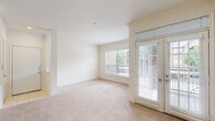 This single-story, one-bedroom, one-bathroom unit offers a thoughtfully organized floor plan that maximizes its compact footprint. The living room serves as the heart of the space, featuring plush neutral-toned carpeting, cream-colored walls, and generous natural light streaming through multiple windows fitted with blinds. French doors open from the living area, further brightening the space and providing outdoor access.

The kitchen is positioned adjacent to the living room with a peninsula-style granite countertop that defines the boundary between the two areas. White cabinetry, white appliances including a range, microwave, and refrigerator, and hardwood flooring give the kitchen a clean, functional aesthetic. A louvered door nearby provides access to additional storage.

The bedroom is a comfortable, well-proportioned room with soft carpeting, a ceiling fan, and a window offering natural light. Direct access to a dedicated closet with built-in shelving and rods provides organized storage. The bathroom features a full tub-shower combination with white and beige checkered tile accents, hardwood flooring, and a vanity with built-in lighting. The overall ambiance of the unit is light, neutral, and move-in ready.