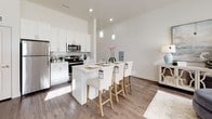 This single-floor residence is designed with a clean, contemporary aesthetic, combining neutral tones, elevated ceilings, and wood-look flooring to create a cohesive and welcoming atmosphere throughout.

The entry area sets a strong first impression with soaring ceilings, a elegant chandelier, and tall windows that flood the space with natural light. The open-concept living area features large windows dressed with roller shades, allowing ample daylight while maintaining privacy.

The kitchen is well-equipped with stainless steel appliances, including a refrigerator, range, and microwave, complemented by white shaker cabinetry, a subway tile backsplash, and a central island with pendant lighting overhead—ideal for both cooking and casual dining.

The bedrooms are carpeted for comfort, each featuring large windows with roller shades and generous closet space. One bedroom includes a dedicated workspace, while another benefits from a walk-in closet with built-in rod storage.

The bathrooms are finished in crisp white tones. One features a full tub-shower combination with brushed nickel fixtures, while the other includes an elongated vanity with ample storage and direct access to a walk-in closet, enhancing functionality throughout.