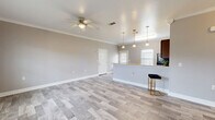 This single-story, 3-bedroom, 2-bathroom home offers a functional and modern layout designed for comfortable everyday living. The open-concept kitchen and living area serves as the heart of the home, featuring light wood-look flooring, crown molding, and a ceiling fan that enhance the bright, cohesive aesthetic. The kitchen is outfitted with rich dark wood cabinetry, granite countertops, black appliances including a refrigerator, range, and microwave, and a peninsula with pendant lighting that provides both prep space and casual seating. The spacious primary bedroom includes a ceiling fan, natural light from slatted blinds, and access to a dedicated closet. The two additional bedrooms mirror the same neutral palette, wood-look flooring, crown molding, and ceiling fans, making each a versatile and comfortable space. Both bathrooms feature tub-shower combinations with tile-look flooring and clean, neutral finishes. A hallway connects the bedrooms and bathrooms, while four closets throughout provide ample storage. The home also includes a utility room and a one-car garage, rounding out a practical and efficient floor plan. Consistent warm-gray tones and white trim carry throughout, creating a cohesive and move-in-ready interior.